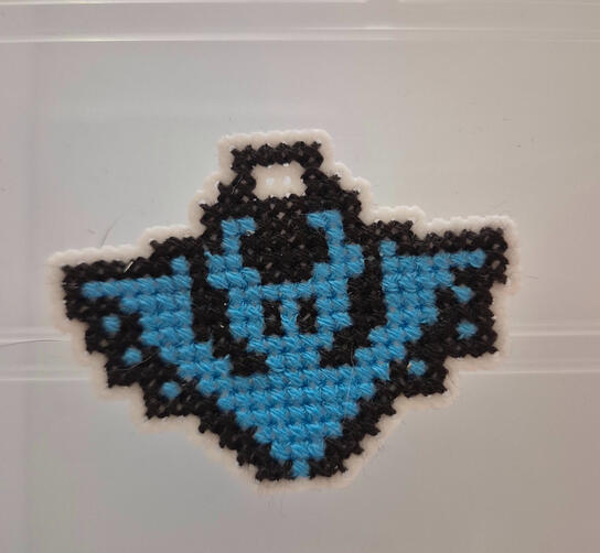 A cross stitched neon bat keychain that glows under black lights